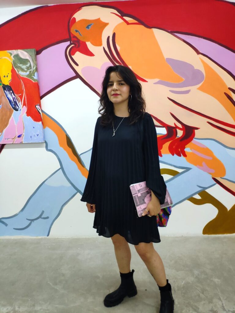 Mujer con cuaderno en la mano vestido negro y mural detrás
