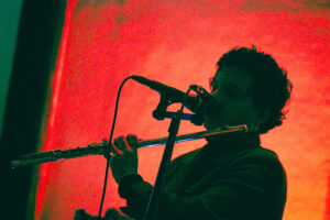 Hombre claroscuro fondo rojo tocando con una flauta es Camilo Ángeles