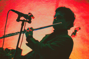 Hombre claroscuro fondo rojo tocando con una flauta es Camilo Ángeles