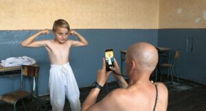 Hombre tomándole foto a un niño sin camisa que hace