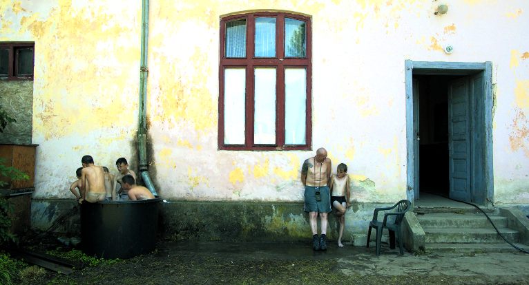 Niños jugando en una tina y hombre al lado de un niño recargados en una casa