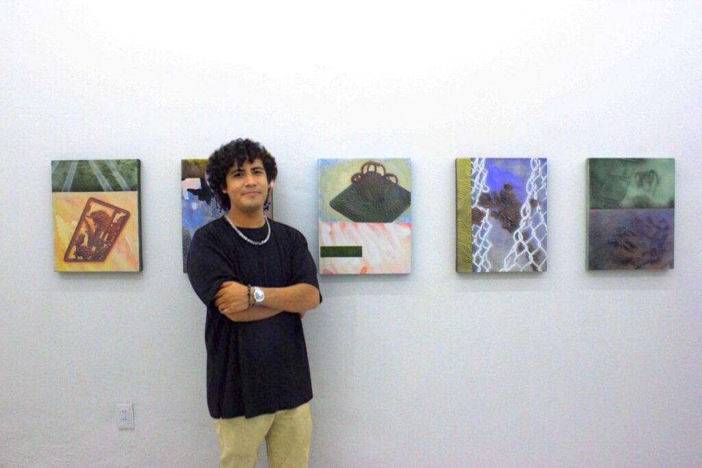 Hombre joven sonriendo brazos cruzados camisa negra de fondo pinturas