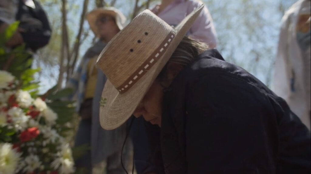 Mujer con sombrero agachada blusa negra personas detrás