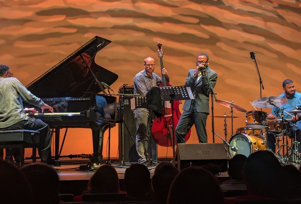 Tres músicos en escenario, piano, contrabajo y trompeta