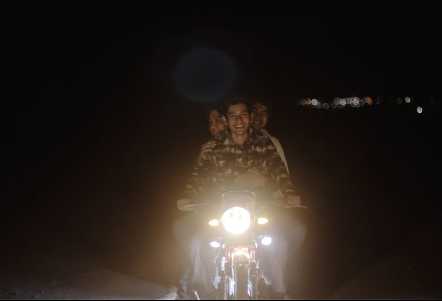 Tres jóvenes encima de motocicleta en la noche Sujo