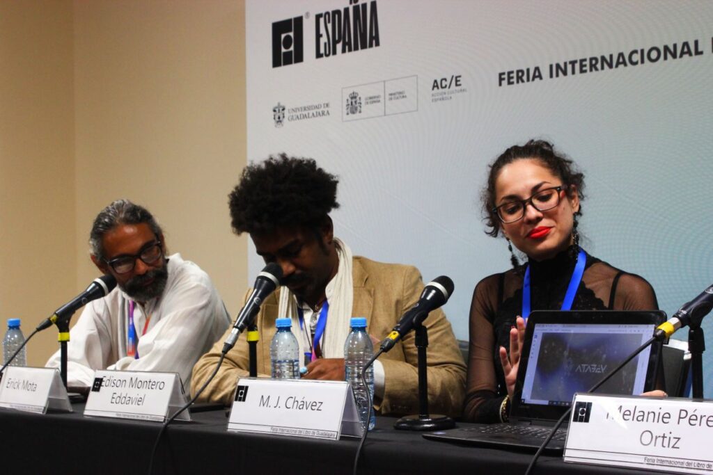 Tres personas en una ponencia: hombre adulto con barba a la izquierda, hombre joven en medio y mujer joven con lentes