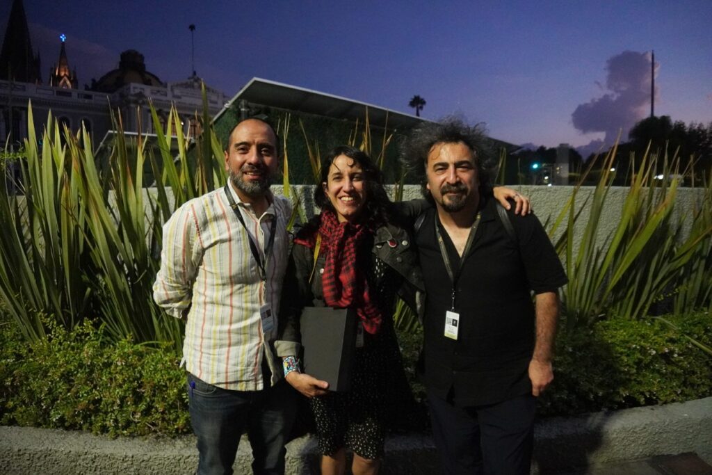 Dos hombres y una mujer tomados de la espalda de fondo plantas