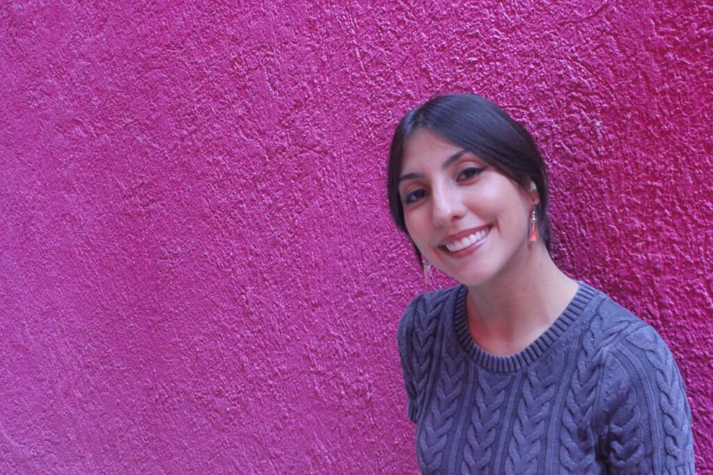 Mujer joven cabello recogido sonriendo recargada en pared