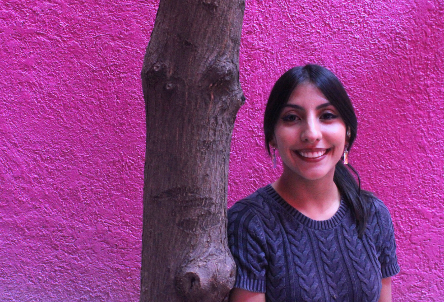Larrisa Rú mujer joven cabello largo recargada en un árbol fondo morado