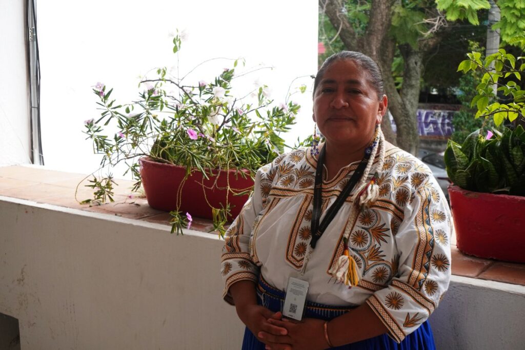 Mujer adulta con vestido tradicional detrás plantas