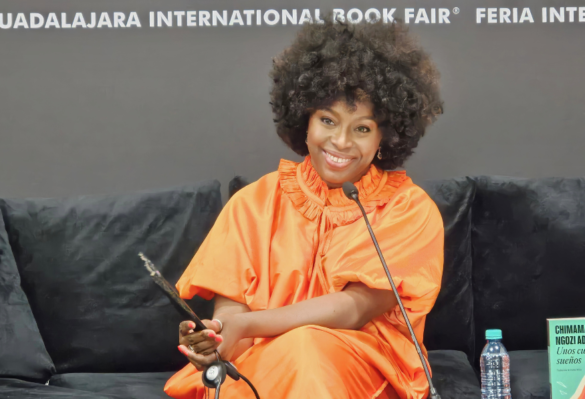 Chimamanda Ngozi Adichie mujer cabello chino, vestido naranja sentada