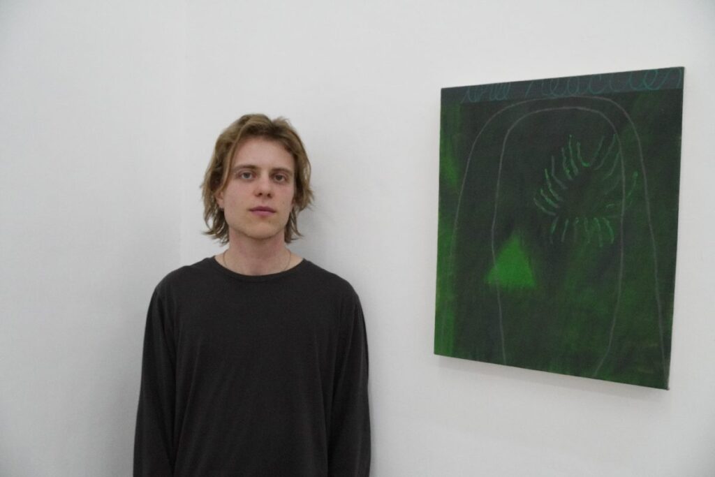 Hombre de suéter negro al lado de pintura